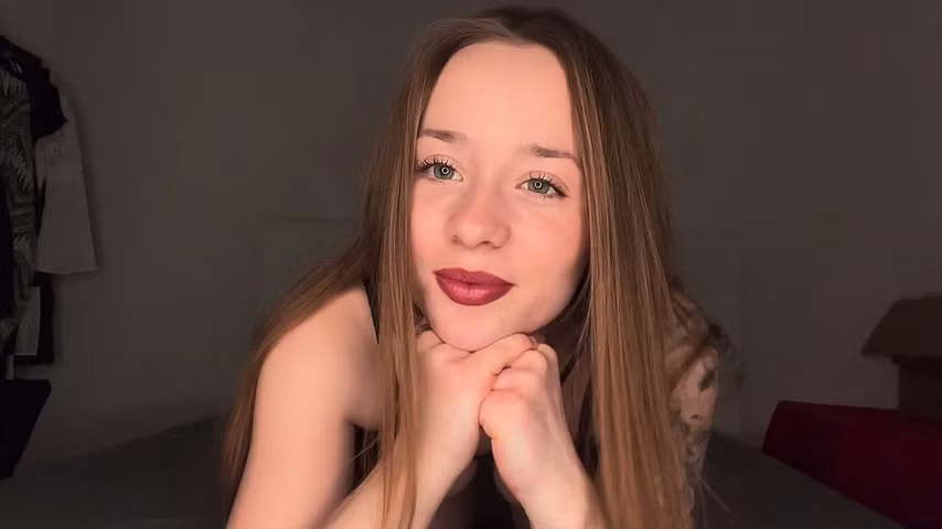 Cerise liegt auf dem Bauch, mit offenen Haaren und rotem Lippenstift, und schaut süß in die Kamera.
