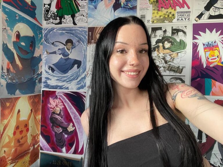 Cassandra Clasen mit offenen Haaren und schwarzem Oberteil vor Posterwand lächelnd