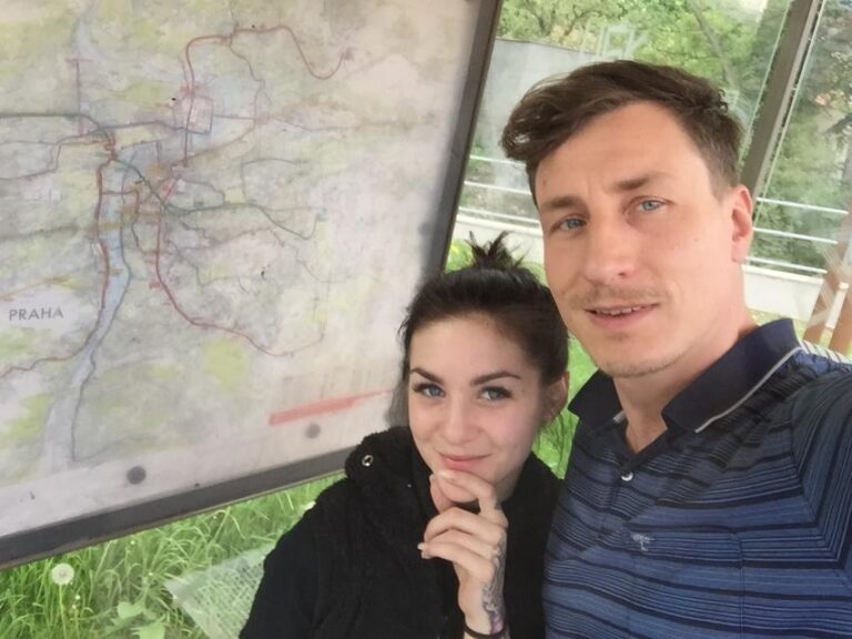 Jason Steel steht mit einem Girl im Arm an einer Bushaltestelle und posiert lässig.