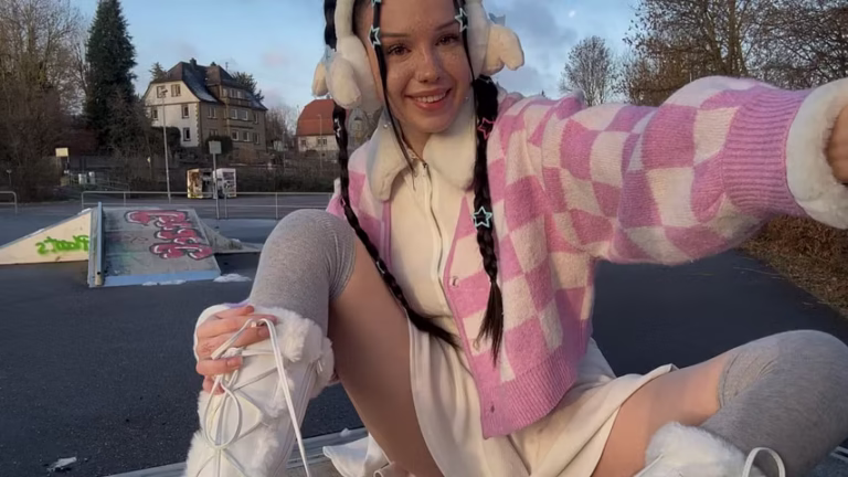 Cassandra Clasen im Skaterpark mit pinker College-Jacke, Minirock und Plüsch-Kopfhörern, lächelnd in die Kamera