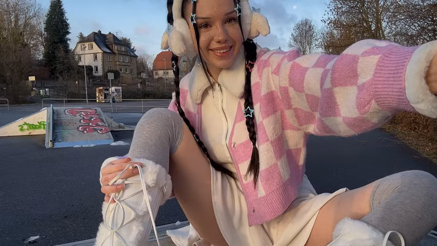 Cassandra Clasen im Skaterpark mit pinker College-Jacke, Minirock und Plüsch-Kopfhörern, lächelnd in die Kamera