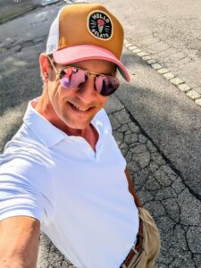 Larry Ragnarök Adler im Selfie-Modus auf der Straße – mit Sonnenbrille, Cap und weißem Poloshirt