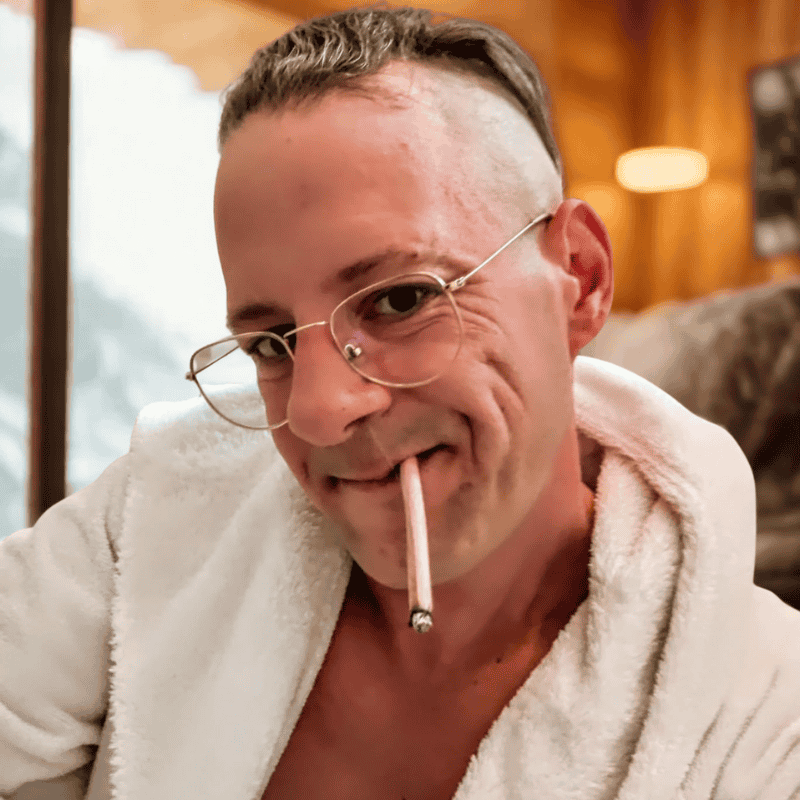 Larry Adler entspannt im weißen Stanglwirt-Bademantel mit Joint im Mund, frischer Frisur und ruhiger Atmosphäre – ein Moment von Klarheit, Haltung und geerdeter Chill-Vibe.