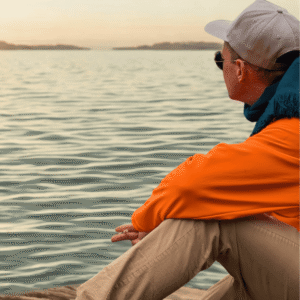 Larry Adler sitzt am Seeufer, blickt in die Ferne und reflektiert Zukunft, Klarheit und neue Wege in einer ruhigen, weiten Landschaft.